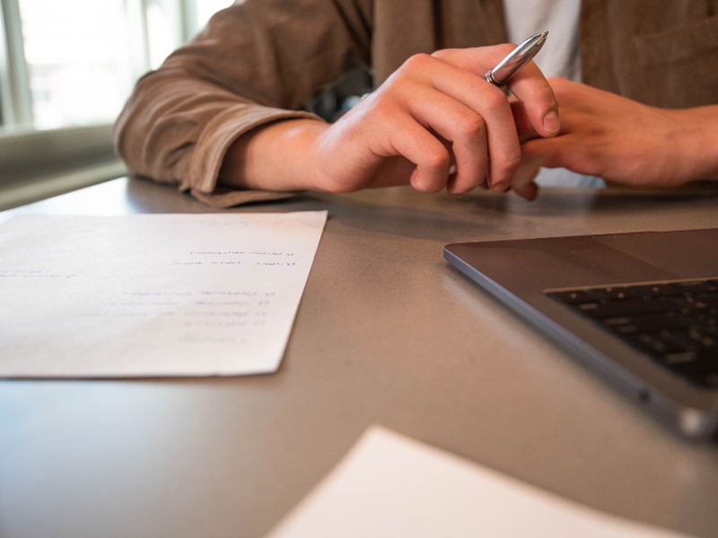 Hands resting on a desk beside a notebook