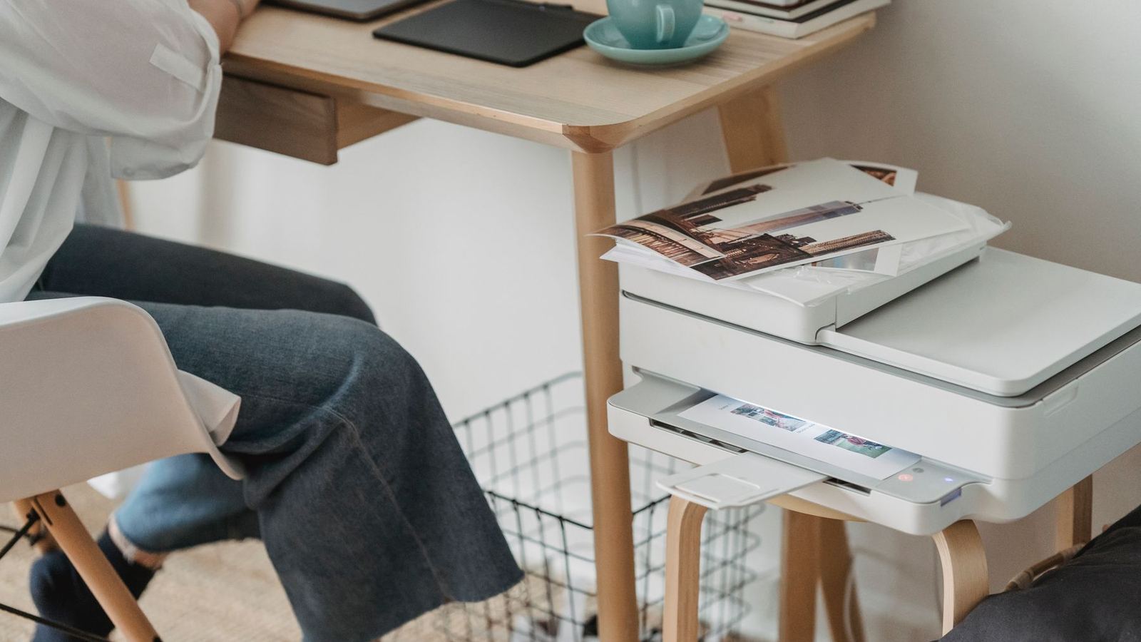 A person seated at a home-office desk beside a printer and laptop