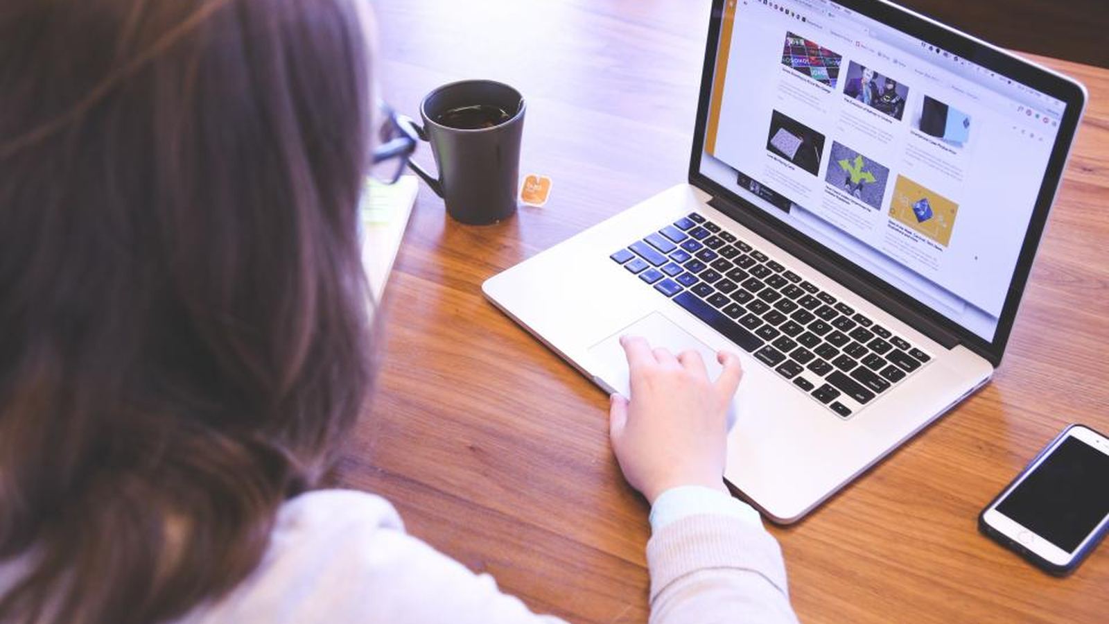 Hands on a laptop at a wooden desk with a coffee cup