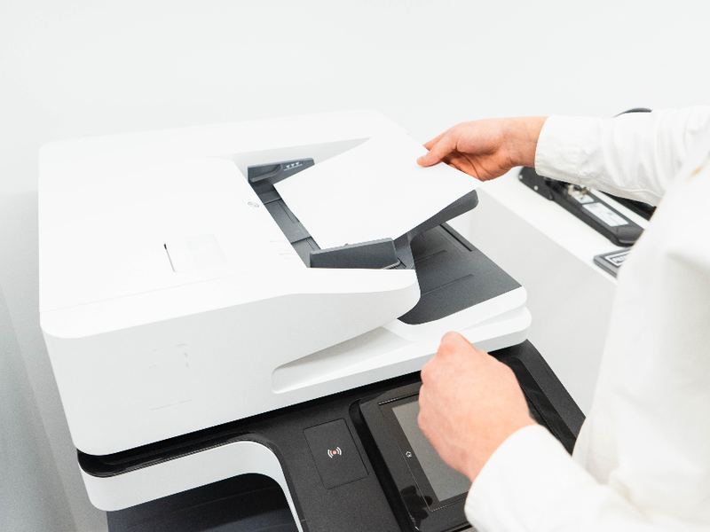 A hand resting on the paper tray of a white printer