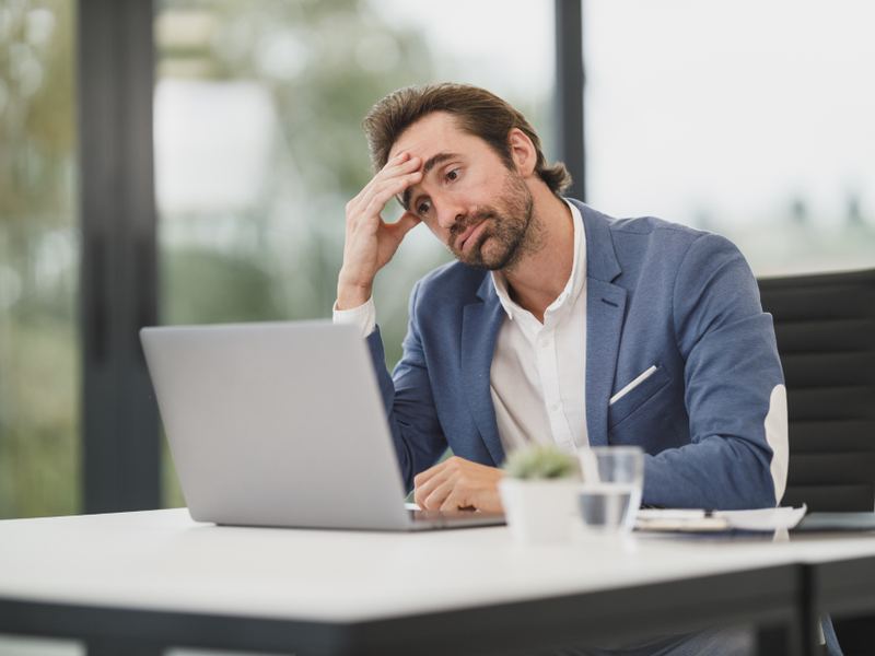 A person sitting at a laptop with a hand to their forehead
