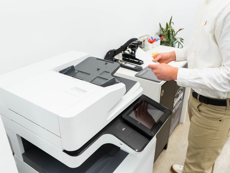 A white all-in-one printer on a desk in a bright office
